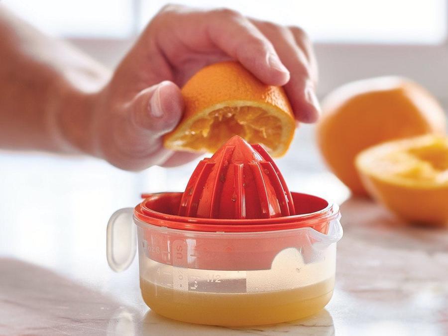 jus d'orange avec le presse-agrumes tupperware all in one mate red juicer avec des oranges en arrière-plan